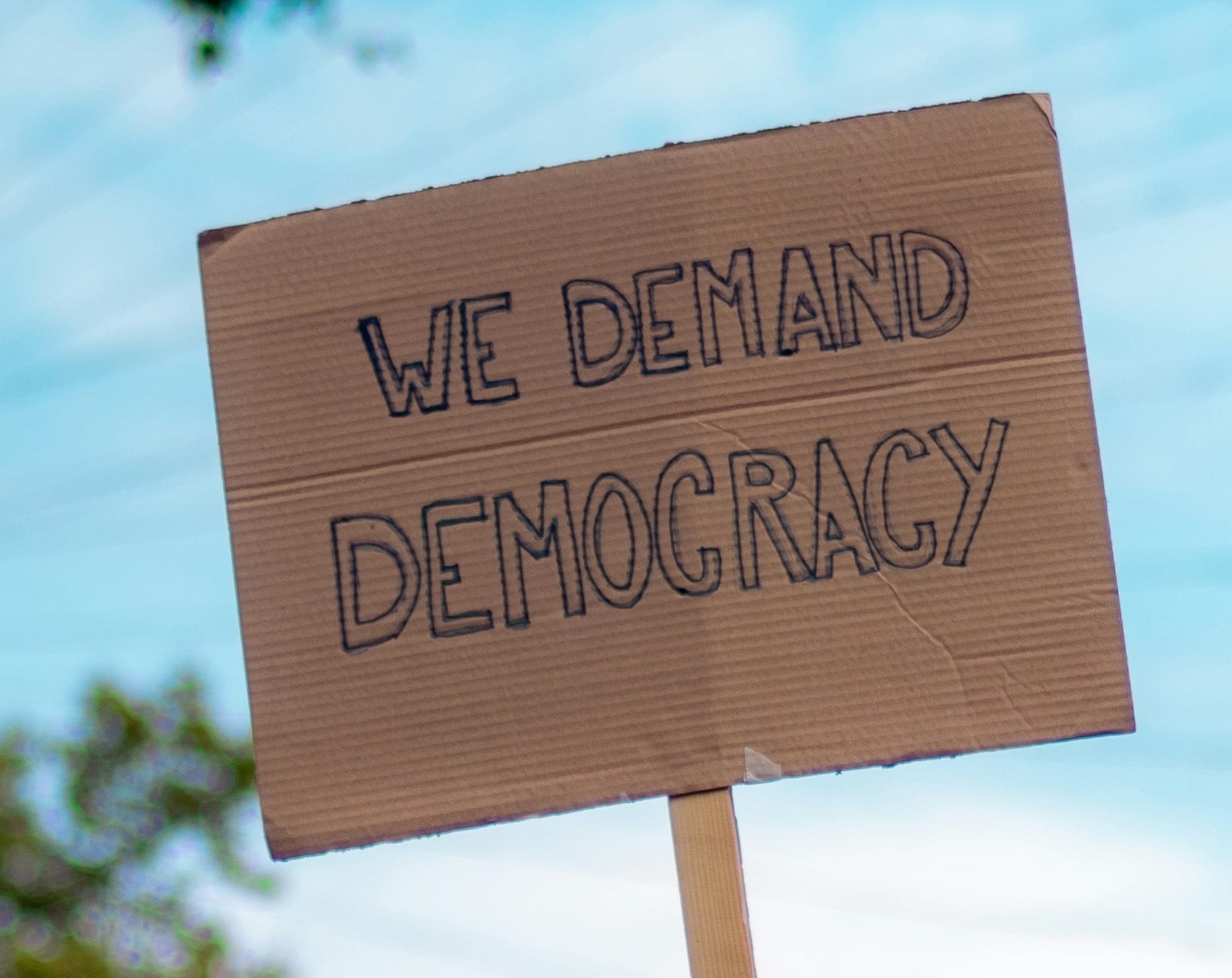 Cardboard sign with We Demand Democracy written on it. Blue sky background