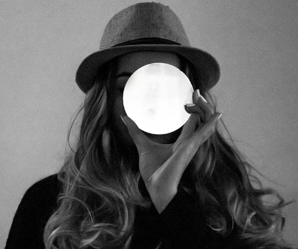 Black and White photo of woman in a hat with long hair, hiding her face behind white orb